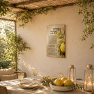 Netilas Lulav vinyl sukkah decoration by Batya with watercolor esrog artwork, hung in a sunlit sukkah above a table set with lemons and glass goblets