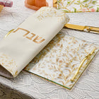 Floral Bird Challah Cover in cream with gold leaf design and leather accents displayed on white surface with decorative items nearby