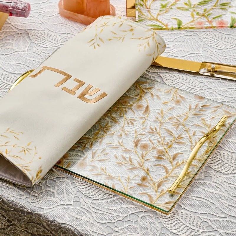 Floral Bird Challah Cover in cream with gold leaf design and leather accents displayed on white surface with decorative items nearby