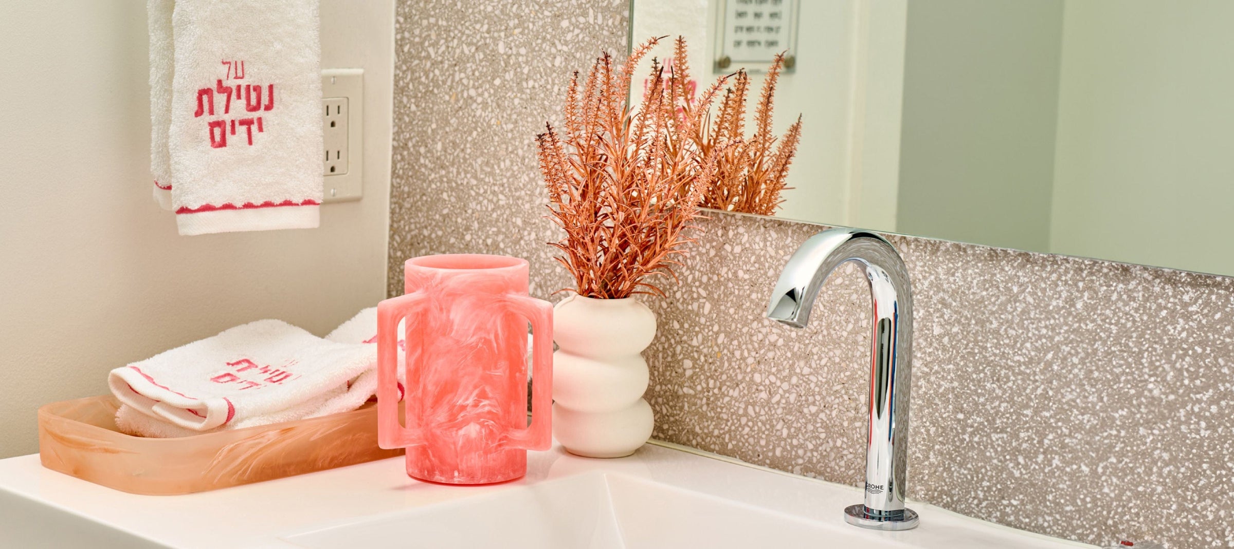 Pink marble-style netilat yadayim washing cup with matching tray and embroidered hand towels, styled on a modern bathroom sink with decorative accents. | Waterdale Collection