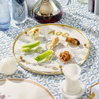 Painted Bais Hamikdash Seder plate with gold accents displayed on a holiday table setting with wine and matzo.