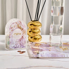Papercut Tzedakah Box in pink with decorative floral design, displayed with candles and Jewish ritual items on white surface.