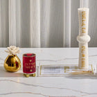 Pearlstone Havdalah set with white ceramic candle holder, red spice box, gold flower diffuser, and prayer card on marble table.
