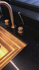Ombre resin washing cup with gold “Al Netilas Yadayim” Hebrew lettering, displayed beside a white embroidered hand towel on a sleek black marble countertop near a modern sink.