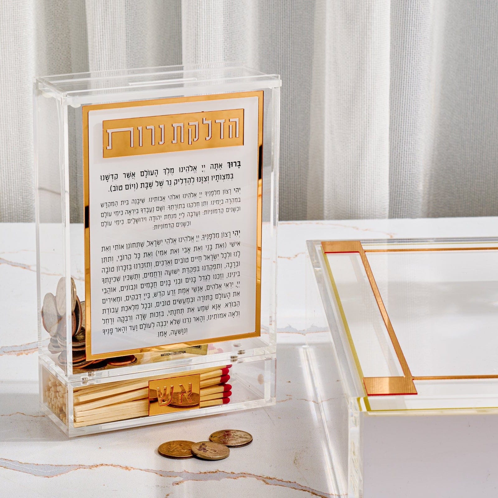 Classic 2.0 Hadlokas Neiros Match Tzedakah Box in clear and gold acrylic, Shabbat candle lighting prayer box with built-in match holder and tzedakah compartment, modern Judaica gift for Shabbos and Yom Tov.