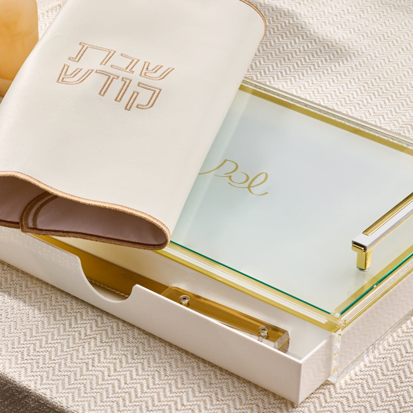 Classic challah board with built-in drawer, featuring a frosted glass cutting surface with gold “Shabbat” detail, gold-tone handles, and a cream “Shabbat Kodesh” challah cover partially draped over the board.