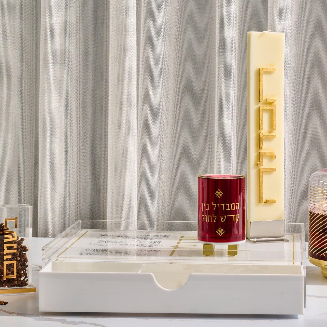 Classic Havdalah tray with built-in drawer, featuring a clear acrylic top with gold accents, displayed with a tall cream Havdalah candle, red besamim holder, and coordinating modern Judaica décor.