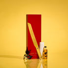 Purim Mishloach Manos gift set featuring a gold serrated challah knife with a clear lucite handle, presented in a tall red gift box alongside a miniature whiskey bottle and dark chocolate.
