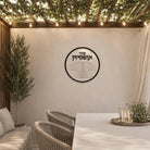 Round clear Lucite Ushpizin sukkah decoration hanging in a modern succah with a Sukkot table, chairs, and potted plants.