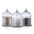 Three glass cloches with metal finials containing dried botanicals, spices, and grains for Cloche Havdalah Set by Waterdale Collection.