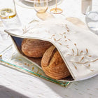 Embroidered leaf challah board and matching pouch set displayed with fresh bread on a white linen tablecloth with table settings.