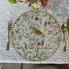 Floral bird acrylic charger plate with yellow songbird and pink cherry blossom design on a white lace tablecloth with gold cutlery.