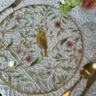 Floral bird acrylic charger plate with yellow songbird and pink cherry blossom design on a white lace tablecloth with gold cutlery.