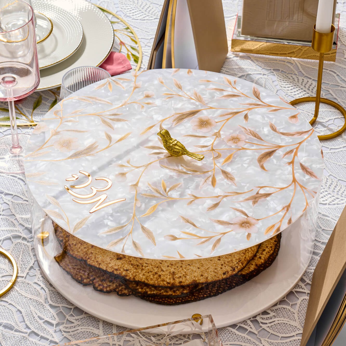 Clear round lucite Matzah holder with an artistic floral vine pattern and a small gold bird ornament on the lid, luxury Passover Seder tableware
