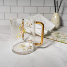 Lucite Washing cup with pink floral design and rose gold handle on a marble countertop with towels in the back - Waterdale Collection