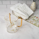 Lucite Washing cup with pink floral design and rose gold handle on a marble countertop with towels in the back - Waterdale Collection