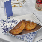 French Toile Challah Pouch Cover in white and gold holding two braided loaves on a table setting with blue toile napkin