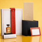 Luxury Mishloach Manot gift box featuring a Leather Hadlokas Neiros Booklet, a white leatherette pouch with a red strap, and a mini Disaronno liqueur.