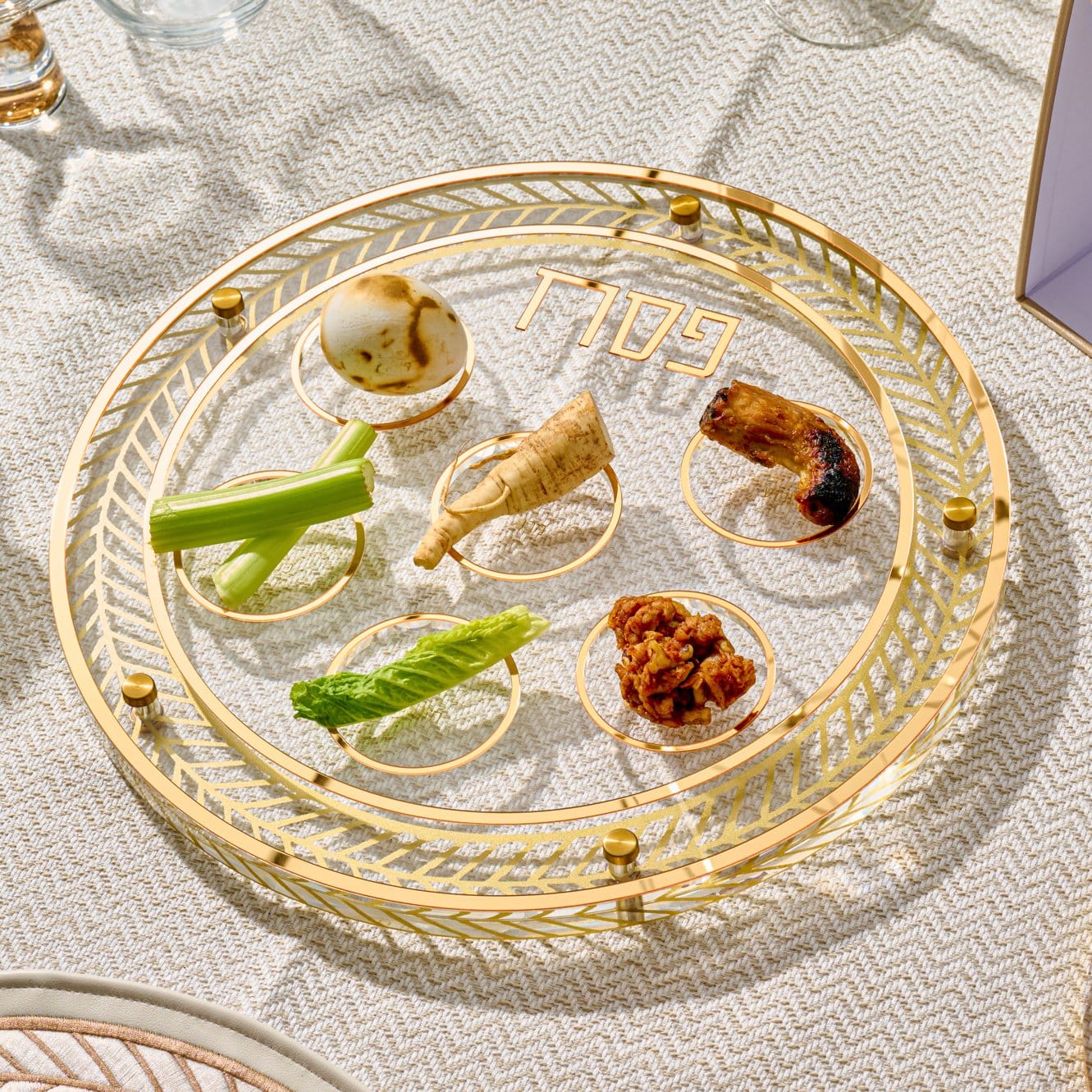 Herringbone Seder plate featuring a clear glass center, intricate gold leaf border, and labeled sections for the Pesach simanim.