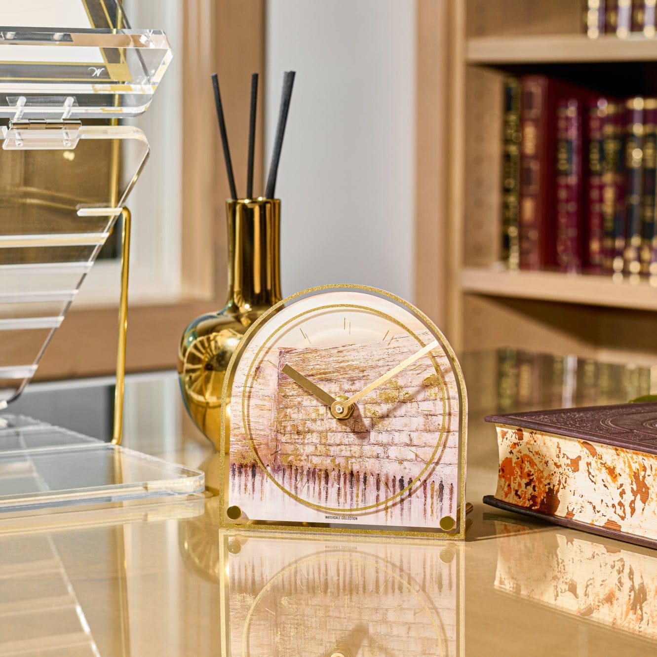 Jerusalem Taupe desk clock featuring a watercolor-style Kosel (Western Wall) illustration in soft taupe tones, framed in a rounded acrylic design with gold trim and gold clock hands, displayed on an elegant desk setting.