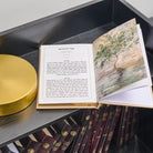 An open Hebrew leather tehillim book with printed text on one page and a tree illustration on the other, displayed on a dark shelf above other bound books.