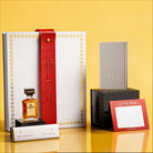 Luxury Mishloach Manot gift box for Purim featuring a white and gold Haggadah with a red leather embossed strap, dark chocolate, and a mini Disaronno liqueur bottle.