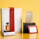 Luxury Mishloach Manot gift box for Purim featuring a white and gold Haggadah with a red leather embossed strap, dark chocolate, and a mini Disaronno liqueur bottle.