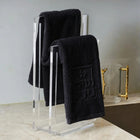 Embossed netilas yadayim towel set displayed on modern metal stand with three folded towels and decorative gold item on shelf.