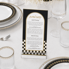 A clear acrylic ONYX KIDDUSH CARDwith a black and gold design, displayed on a white tablecloth surrounded by plates, glasses, and a fork.