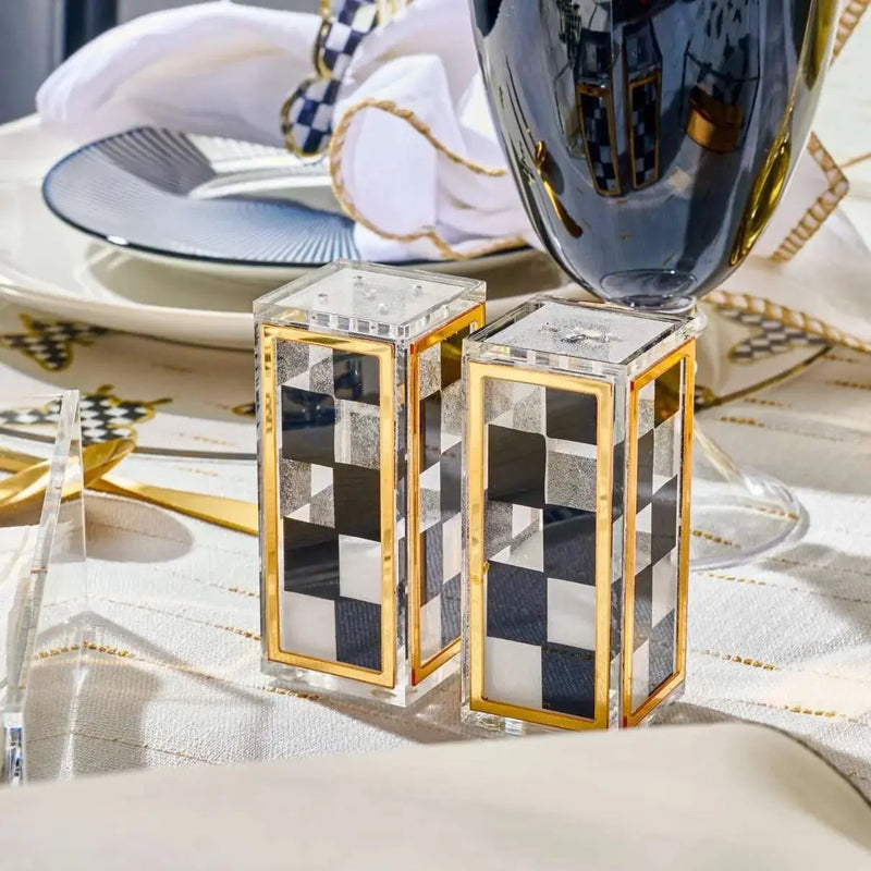 Pair of black onyx salt shakers with gold-tone metal accents and checkered design details, displayed on white tabletop setting.