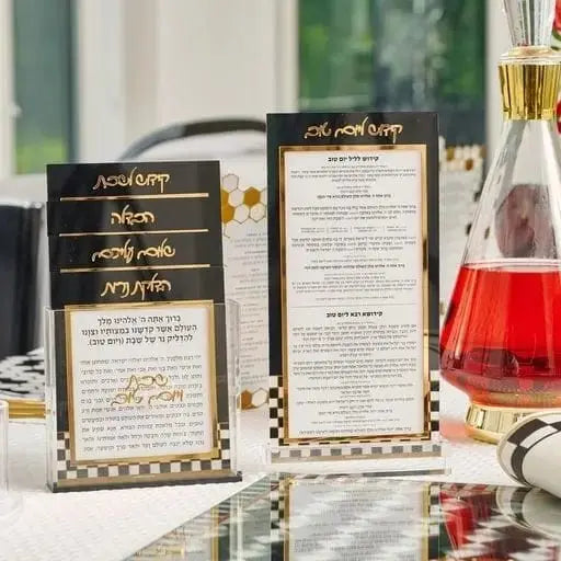 Onyx Shabbos Card Set by Waterdale Collection displaying black lucite cards with gold text, arranged on a checkered surface with candles and wine in background.