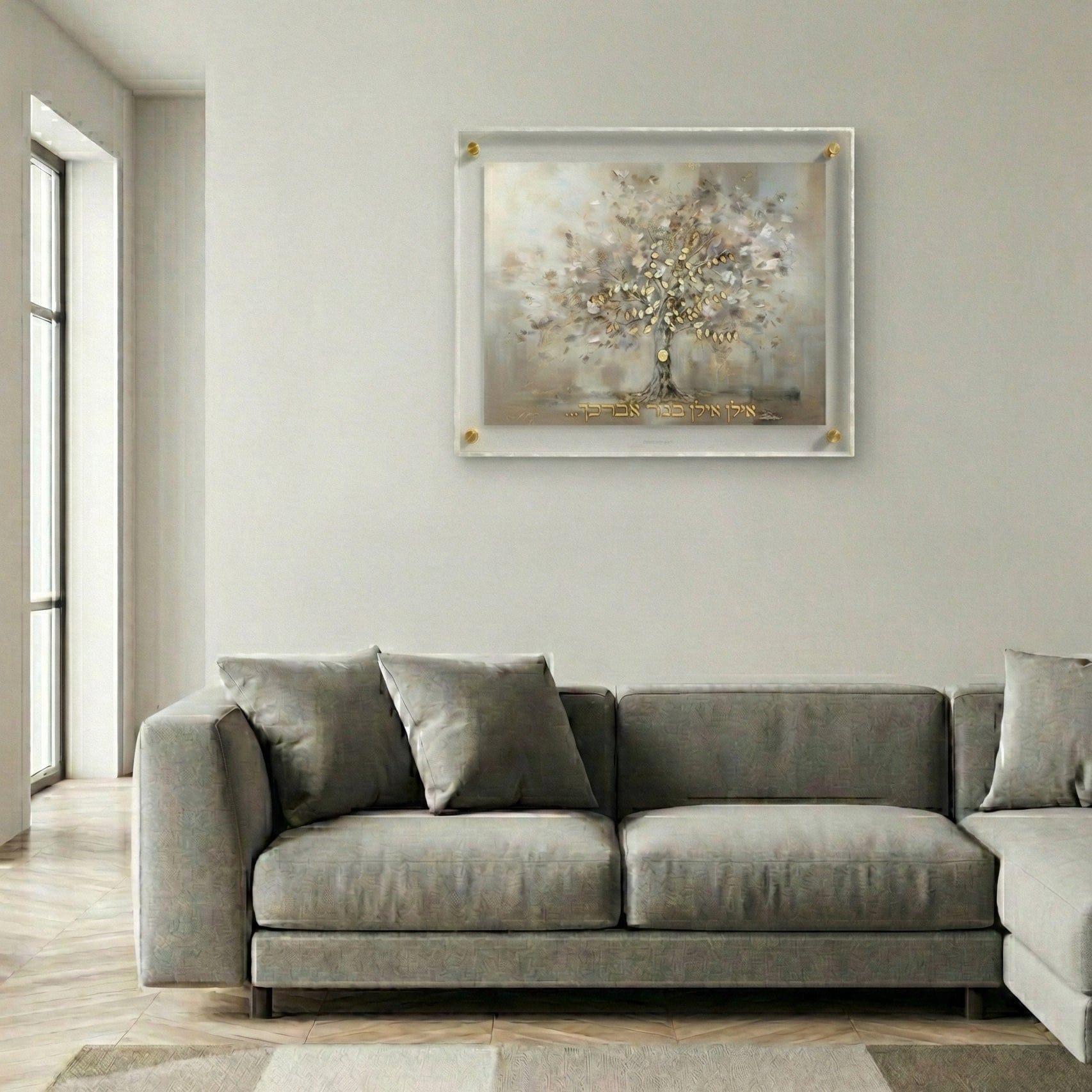 Painted by Batya framed abstract family tree wall art featuring soft neutral tones, gold leaf details, and Hebrew text, displayed above a modern gray sofa in a contemporary living room.