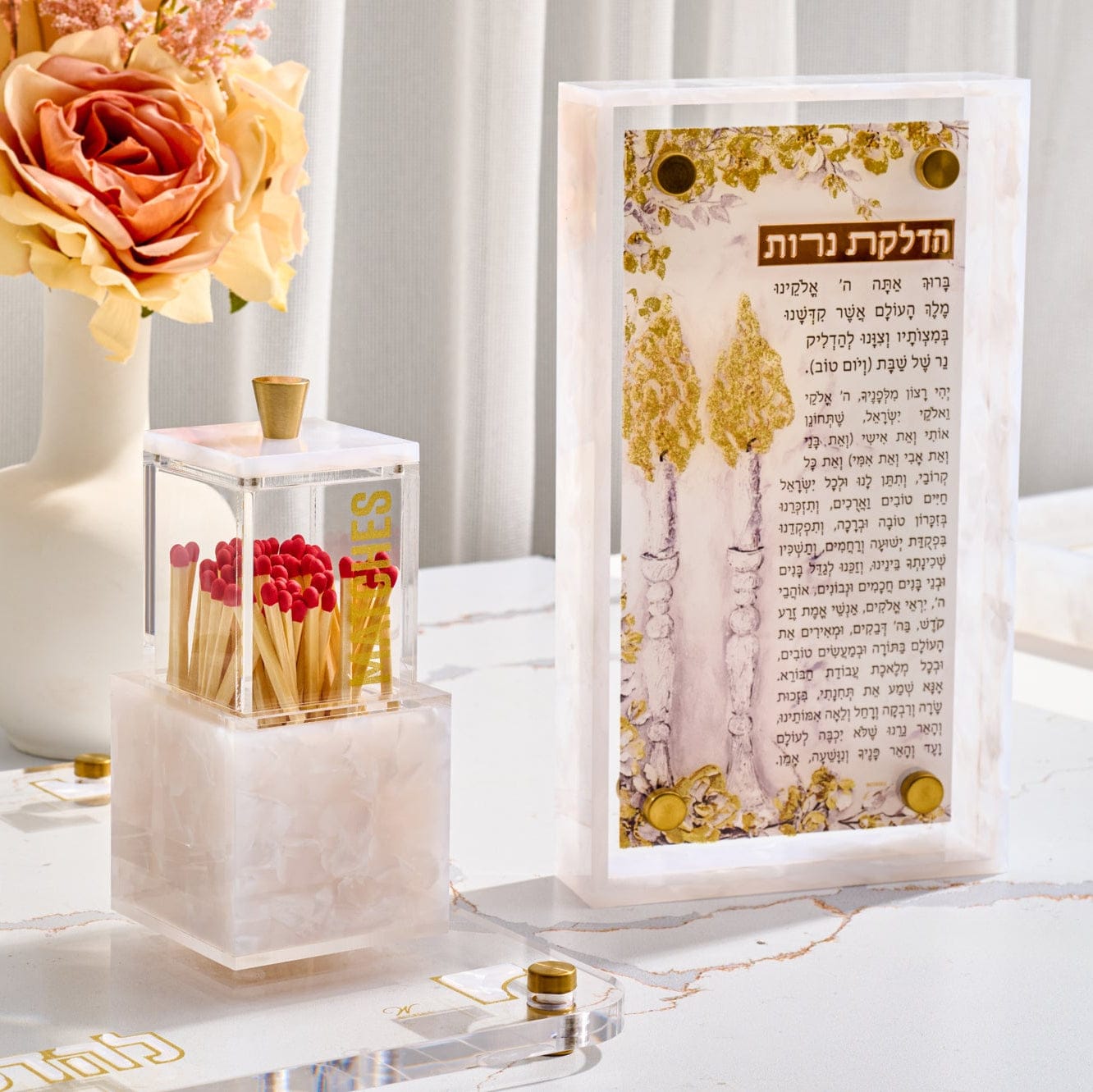 Painted Frame Hadlokas Neiros featuring elegant Hebrew candle-lighting text set against soft blush and gold artwork, encased in a clear lucite frame with pearlstone-style detailing and gold accent hardware for a Shabbos display.