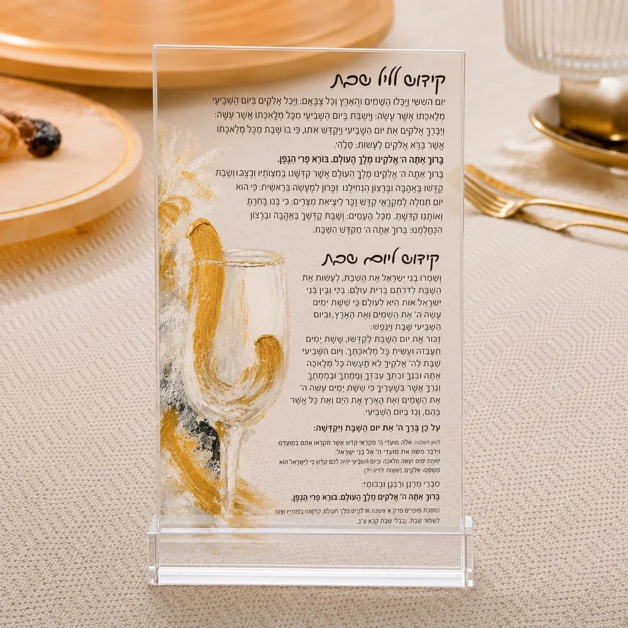 A clear acrylic stand holding a printed Hebrew prayer card, photographed on a beige fabric surface with a blurred plate of food in the background.