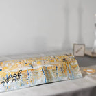 Gray and gold painted Kosel Challah Board and Cover Set displayed on white bedding with blurred candles in background