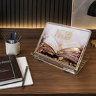 Lucite tabletop foldable shtender with painted sefer design that says Vehagisa Bo Yomam V'layla with gold accents on it. Set on a desk lifestyle display with sefer and pens.