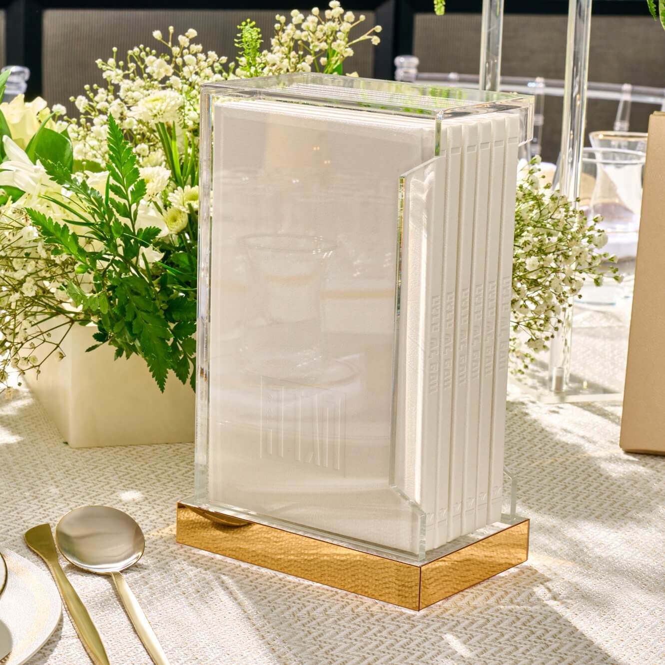Modern lucite bencher holder featuring six white embossed Zemiros booklets on a reflective gold base, luxury Shabbat and holiday tableware.