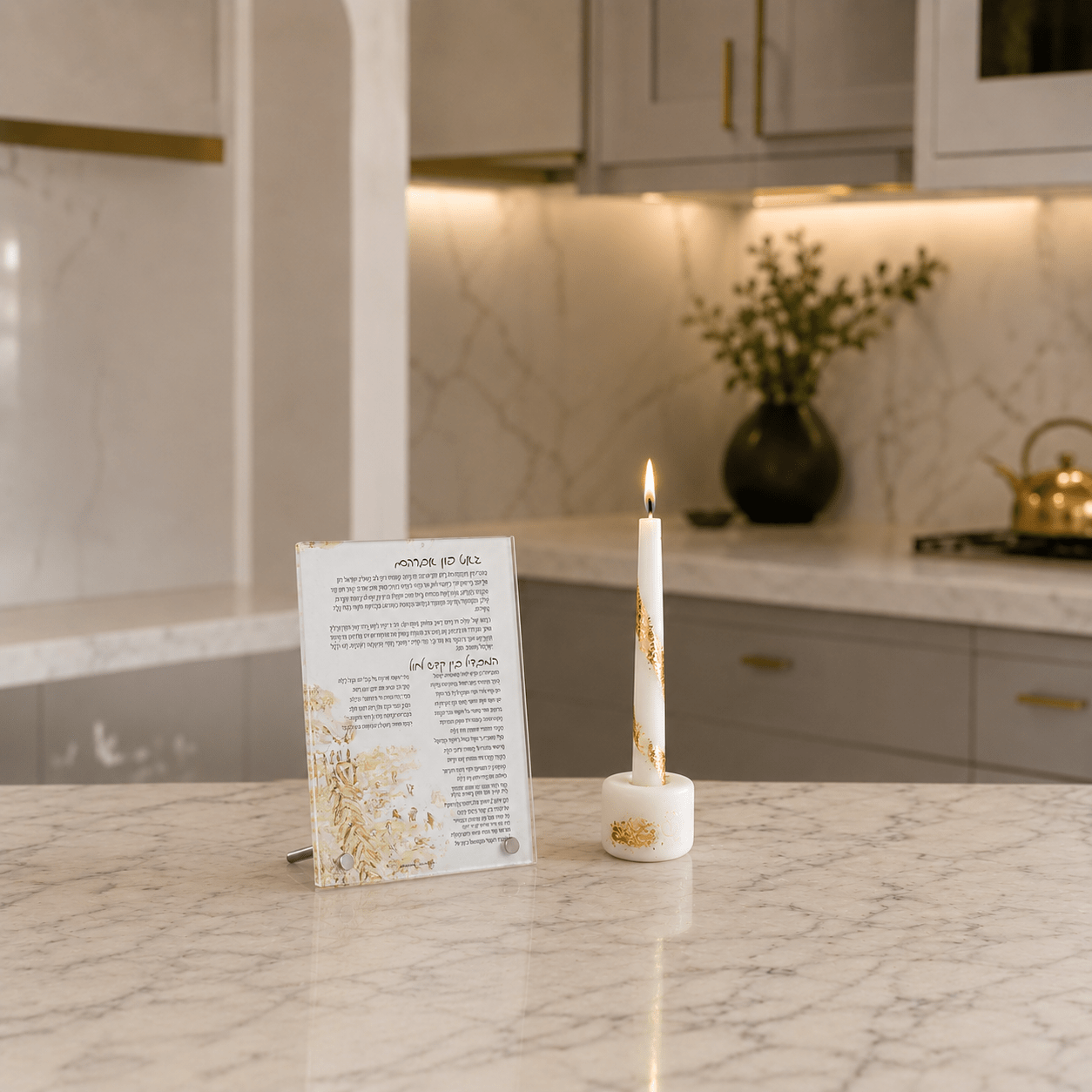 A white candle in a white holder with gold accents stands on a marble countertop next to a printed card in a modern kitchen setting.