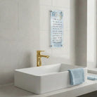 Painted Yosefa Kosel Asher Yatzar featuring elegant Hebrew text set against a serene blue-toned Kosel artwork with subtle gold accents, mounted in a sleek lucite wall frame on a modern bathroom.