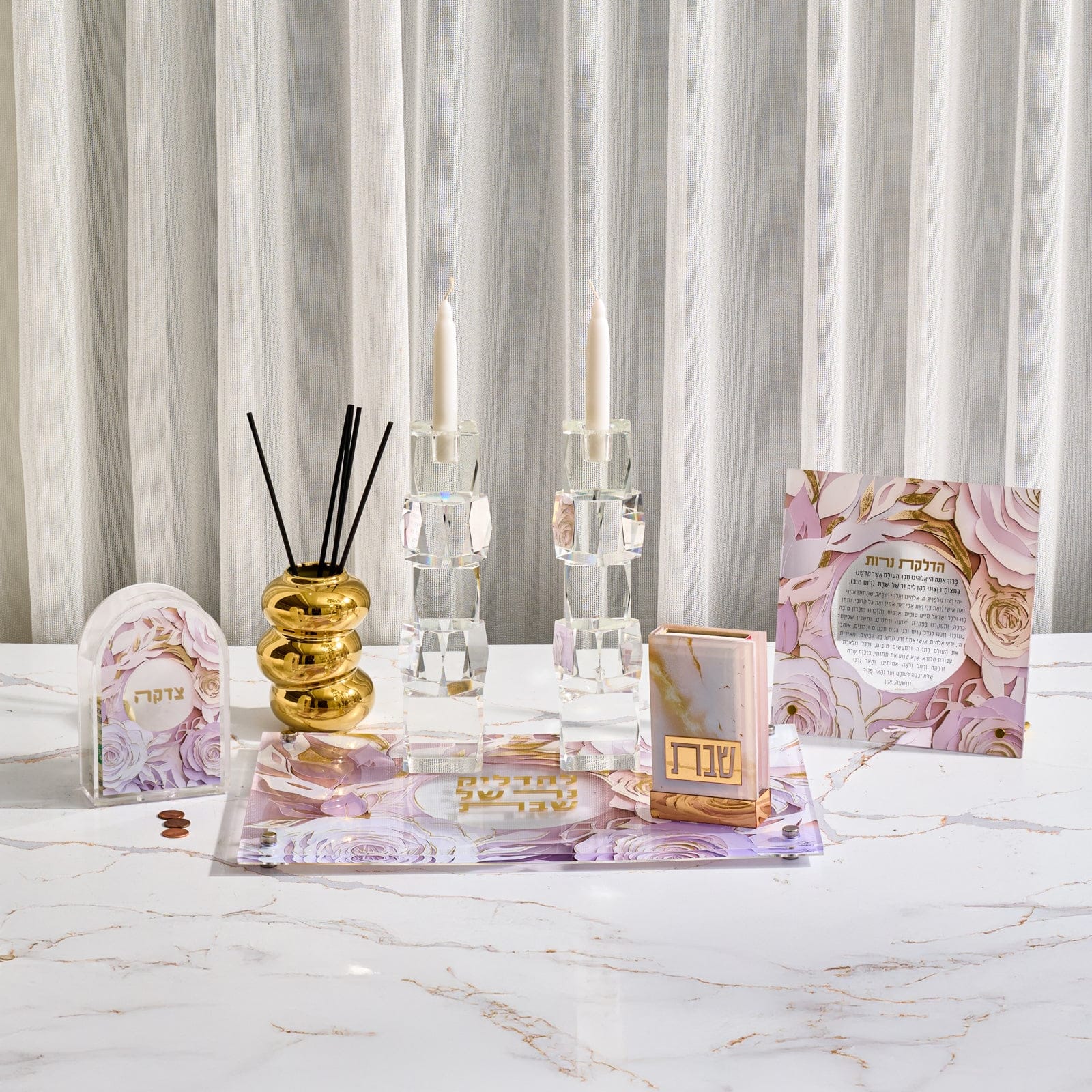 Papercut hadlokas neiros set featuring crystal candle holders and a purple floral acrylic tray alongside a matching tzedakah box prayer card and gold accents on a marble table.