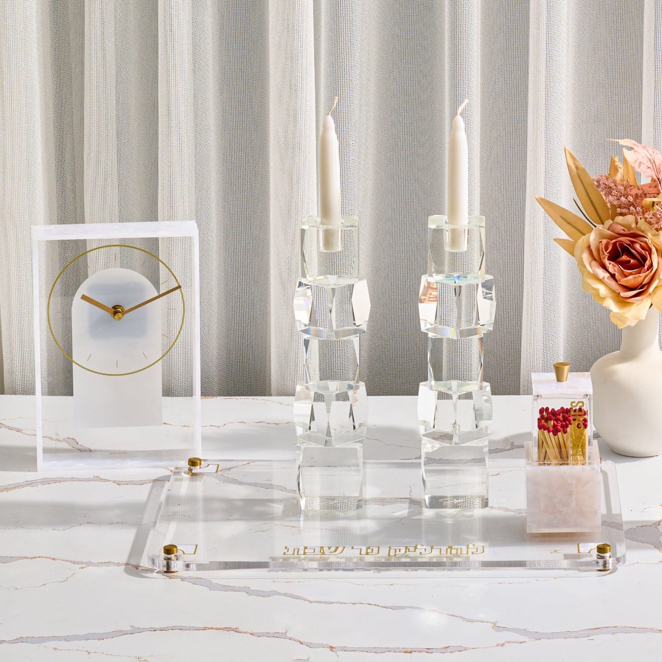 Pearlstone hadlokas neiros set featuring modern crystal candle holders and an acrylic matchbox on a crushed marble and acrylic tray with gold accents on a marble table.