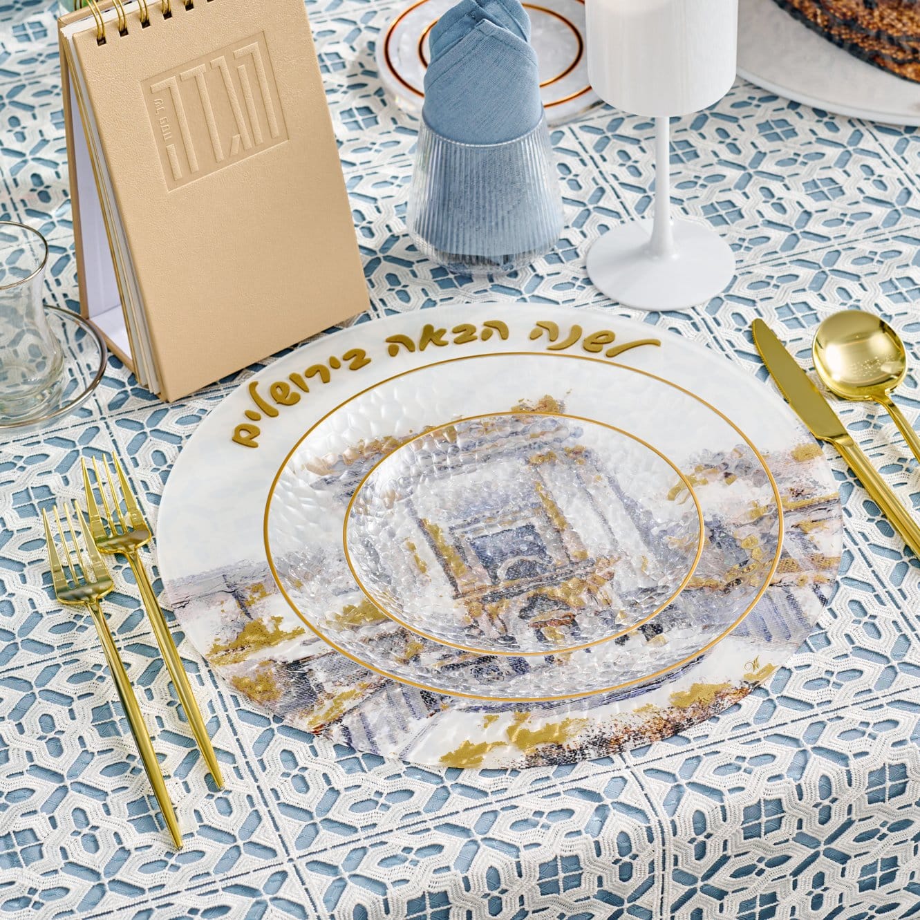 Pesach Bais Hamikdash charger with Jerusalem illustration and gold Hebrew lettering displayed on a blue patterned Seder table with gold flatware and glassware.