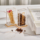 Pillar besamim holder set in clear acrylic with gold lettering, one filled with whole cloves and the other holding wooden matches, displayed beside a coordinating Havdalah tray.