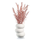 White sculptural donut vase with pink faux floral stems.