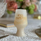 Elegant cream-colored marbled resin Kiddush cup with gold Hebrew lettering "Borei Pri HaGafen" on a white lace tablecloth.