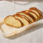 Slices of golden-brown artisan bread arranged diagonally on a translucent rectangular servingresin tray over a textured beige fabric surface.