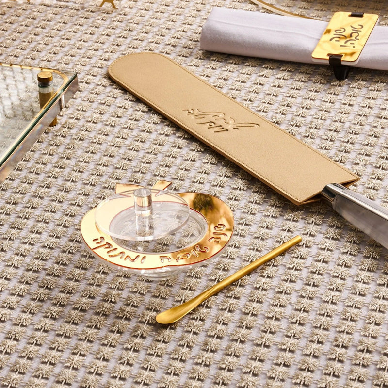 Rosh Hashana tablescape with gold accents, beige linen napkin, place card holder, and decorative elements on neutral textile background.
