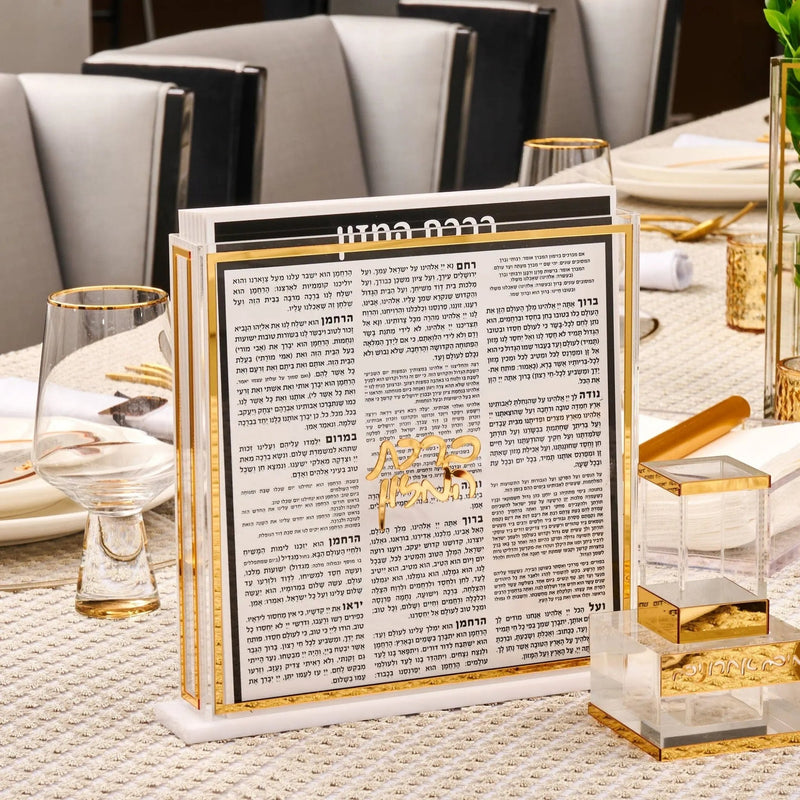 Rosh Hashana tablescape with Hebrew text menu card, gold candlesticks, and place settings on white table linens