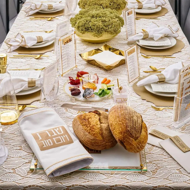 Rosh Hashanah 2024 Classic 2.0 tablescape with formal place settings, gold accents, round challah bread, and green floral centerpiece on white linens.