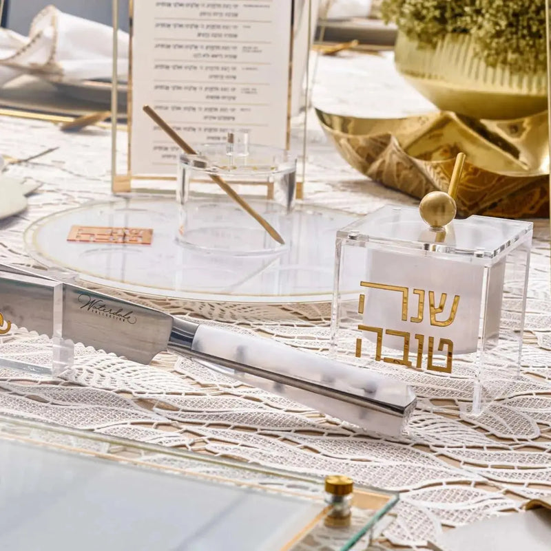 Rosh Hashanah 2024 Classic 2.0 tablescape featuring gold accents, architectural models, and place settings on white surface with blueprints and design materials.